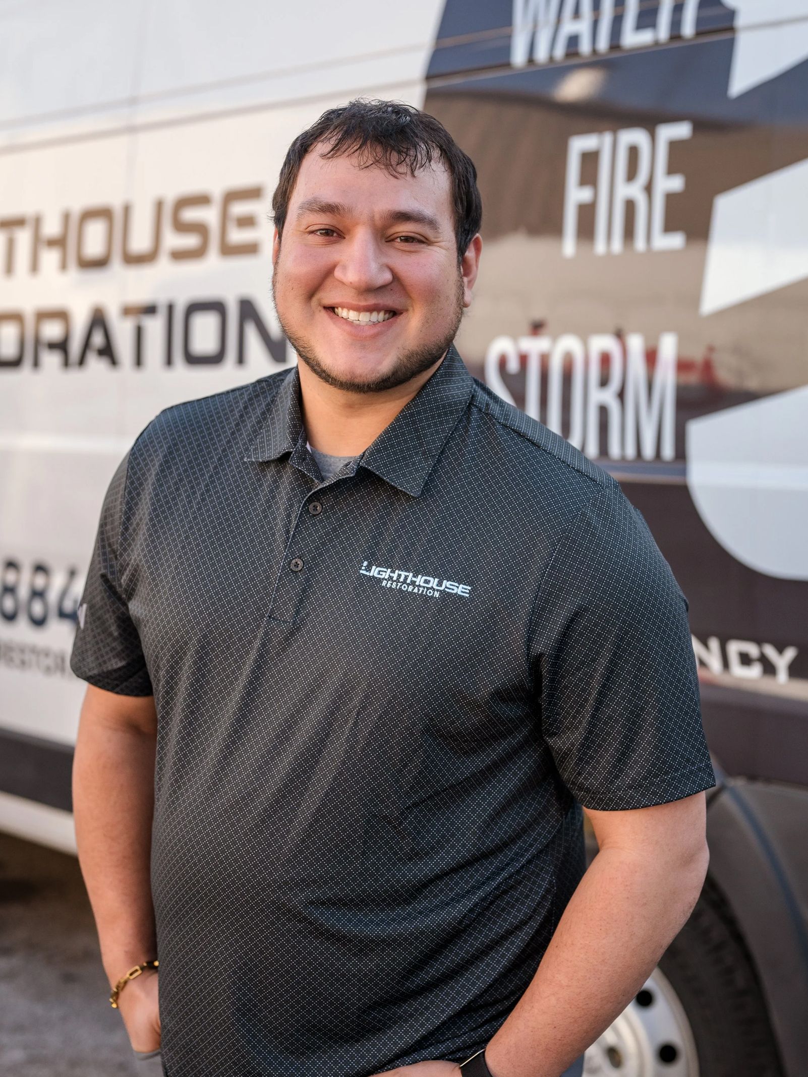 Smiling person in a black patterned polo standing beside a fire and water restoration truck
