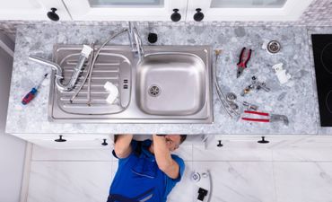 A plumber is fixing a sink in a kitchen