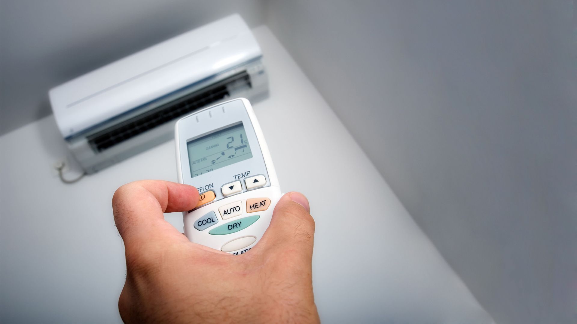 Hand holding air conditioner remote, pointing towards wall-mounted unit, set to 23 degrees.