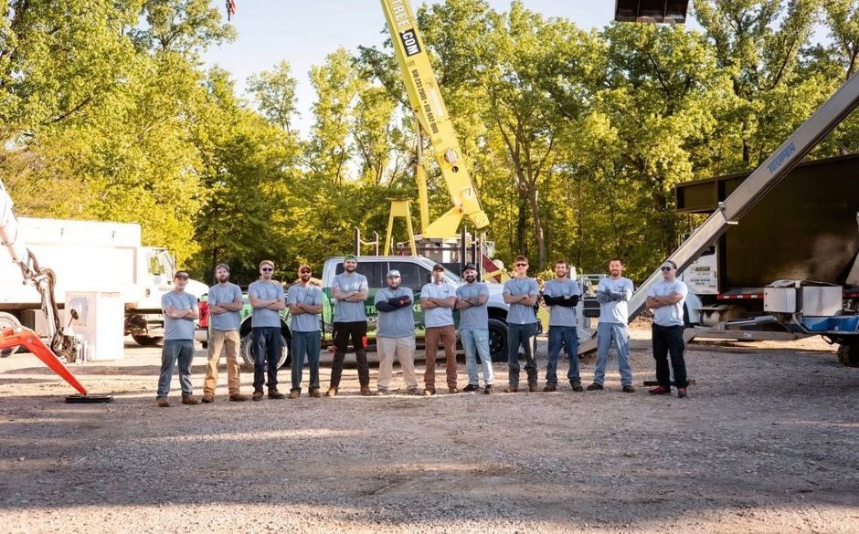Workers stand in a row at an outdoor construction site beside a crane and truck.
