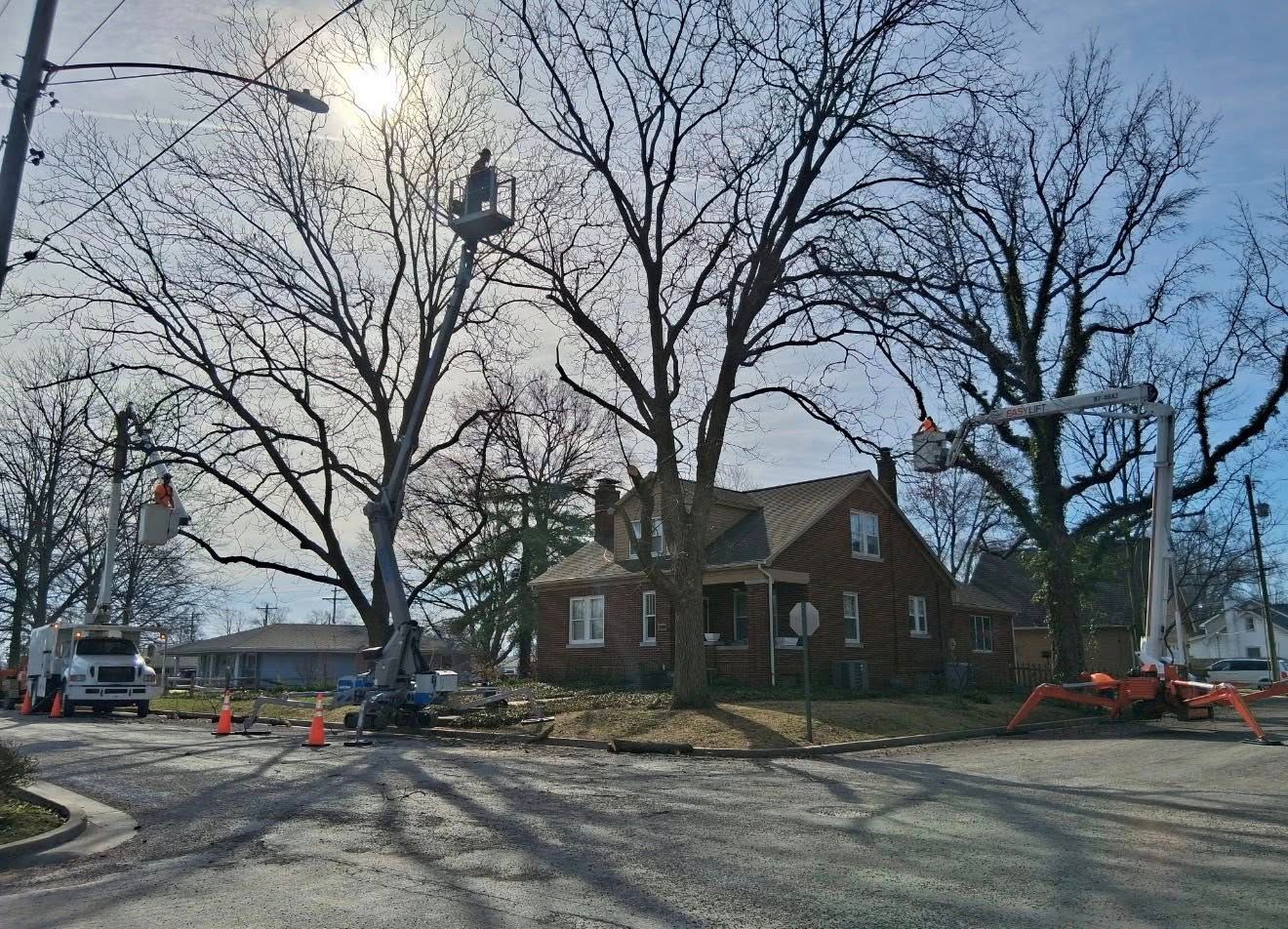 Brick house beside a road with leafless trees, construction equipment, and a bright sun in a winter scene.