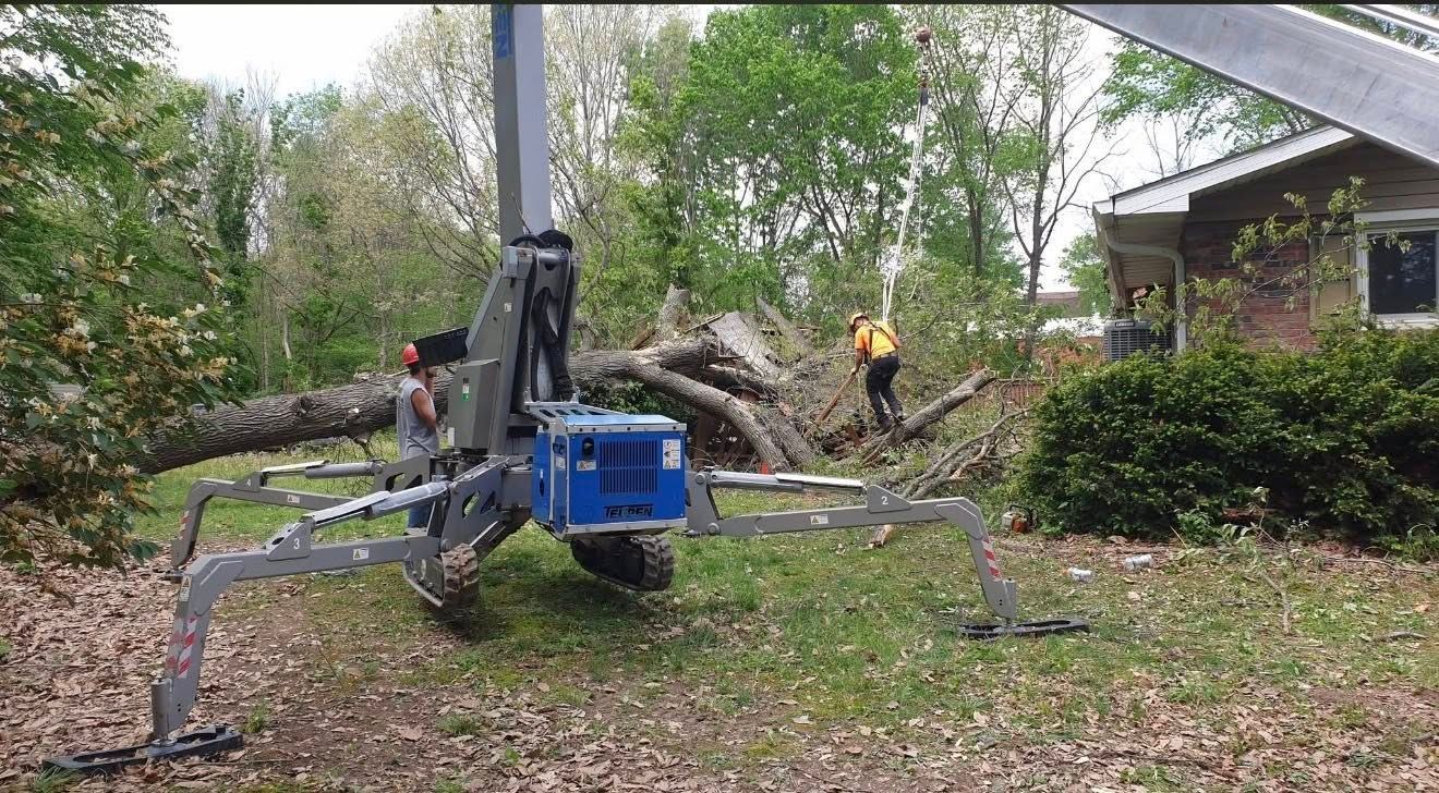 Spider-like utility robot in a yard lifting a fallen tree near a house.