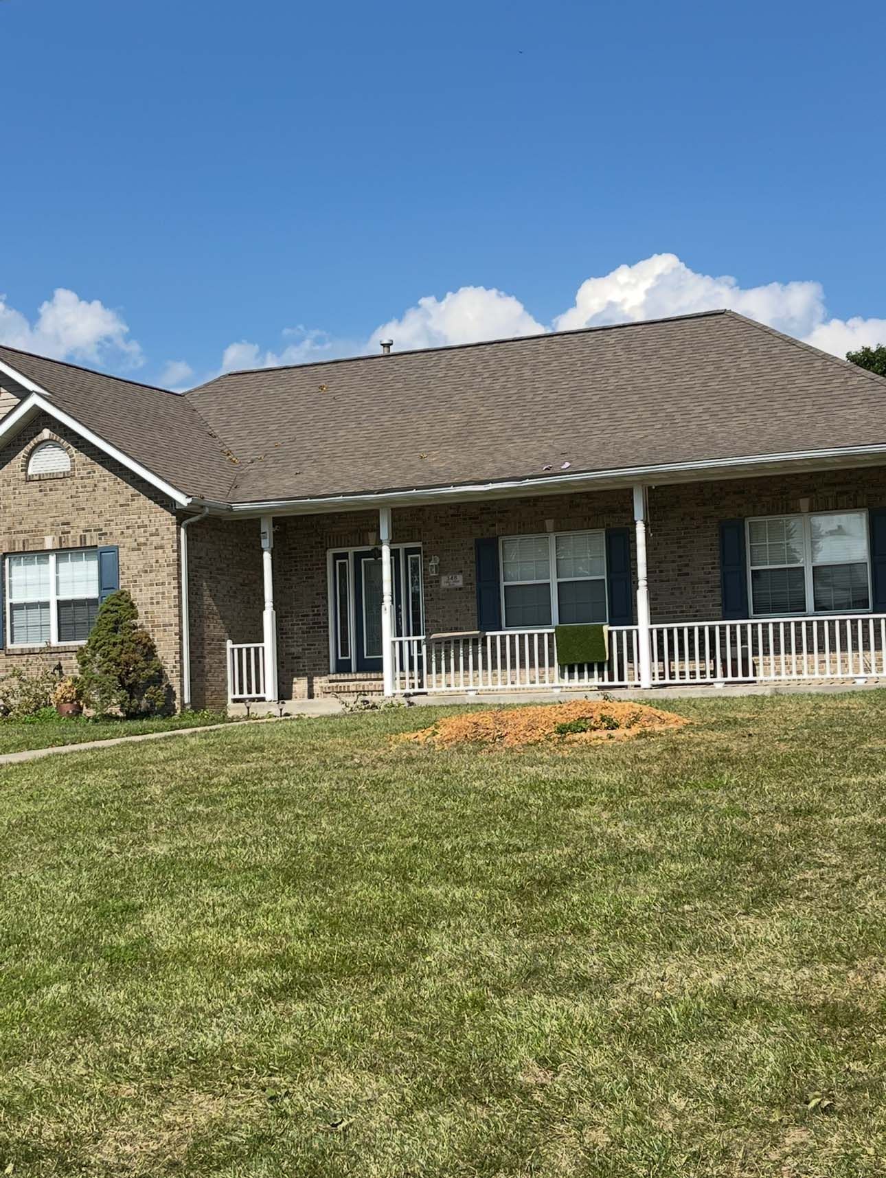 Brick ranch house with a porch on a sunny day. Green grass and blue sky.