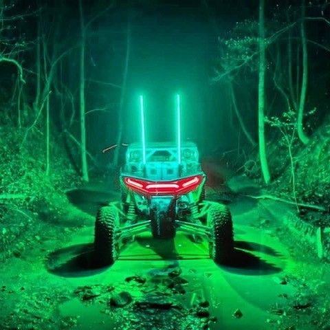 An ATV with green lights is parked in the middle of a forest at night