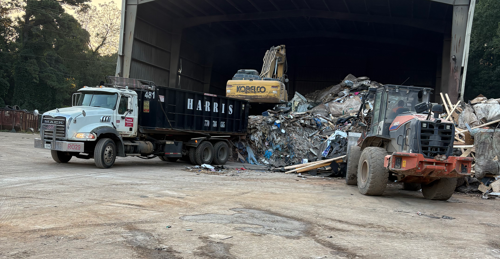A truck and tractor in a metal recycling facility, with an excavator in the background.