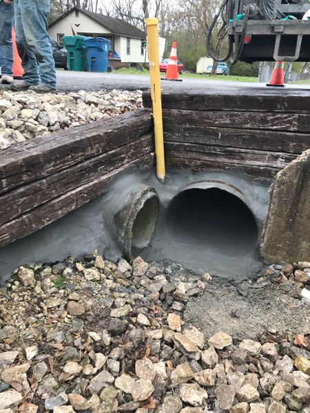 Construction site drainage culvert with exposed pipes, gravel, and a yellow measuring pole at the opening