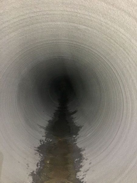 Inside a cylindrical pipe, looking toward a dark opening with a wet stain along the bottom edge