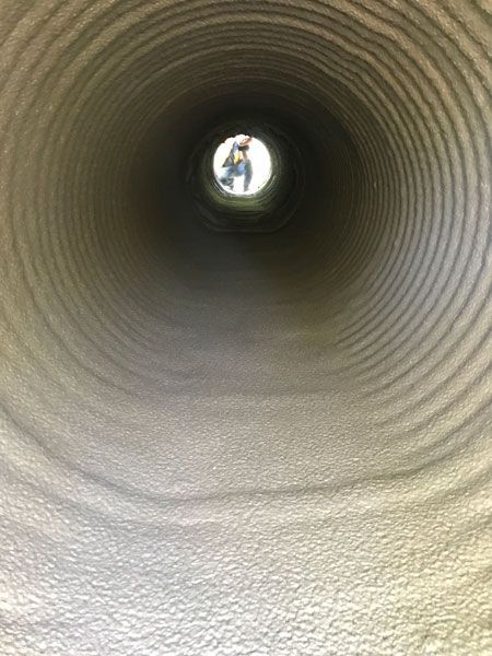 Inside a large concrete pipe, a small person is visible at the far opening.