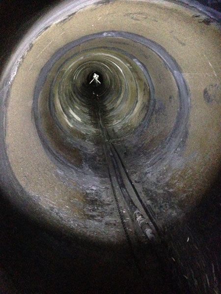 Inside view of a circular pipe or tunnel with a cable running along the bottom toward a distant light.