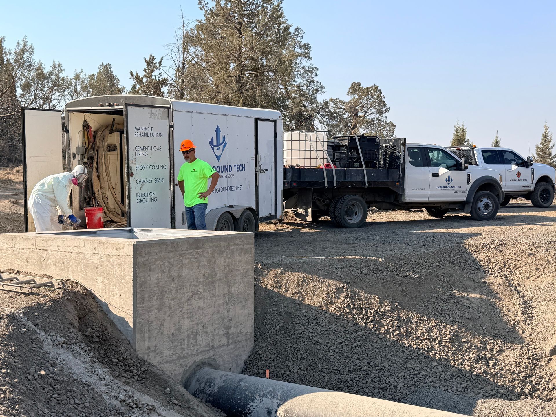 Workers and trucks beside a white utility trailer at a gravel construction site