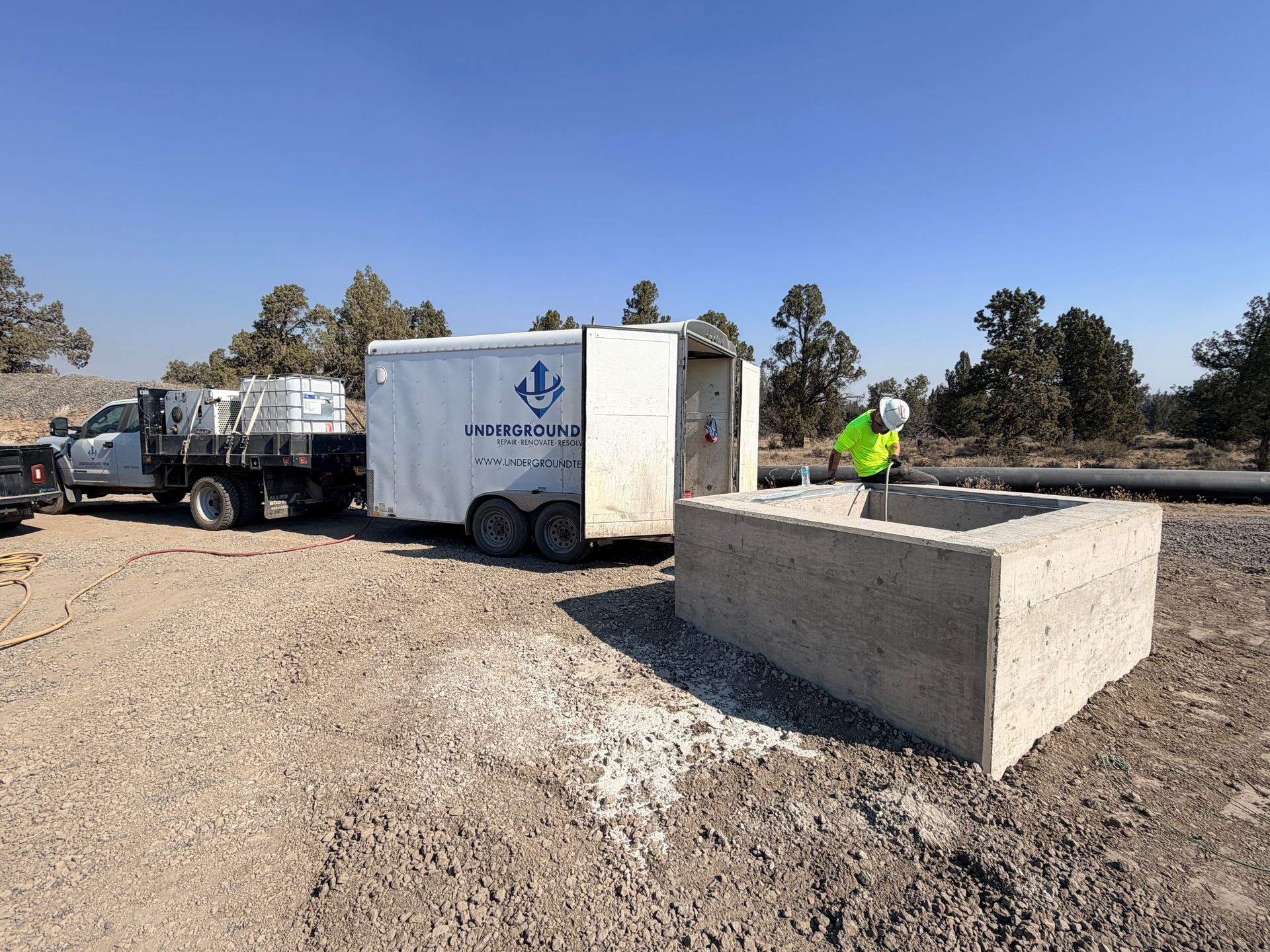 Worker in neon vest beside a trailer and concrete barrier at a roadside construction site.