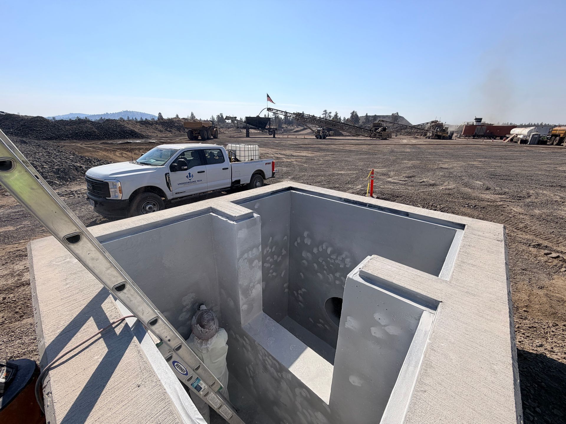 Concrete utility vault under construction beside a white pickup truck on a gravel lot.