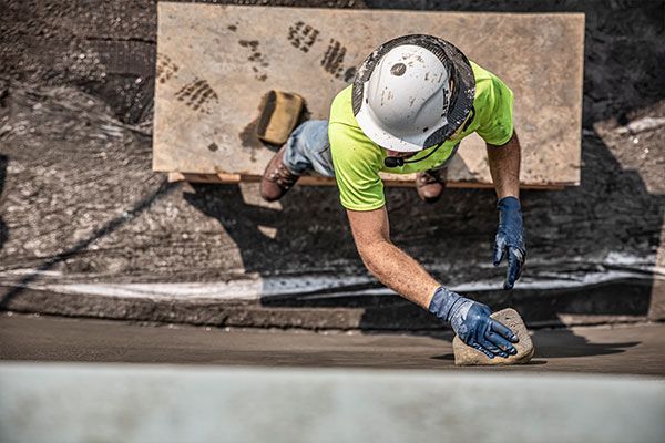 Construction worker painting a wall edge with a brush from a scaffold, seen from above.