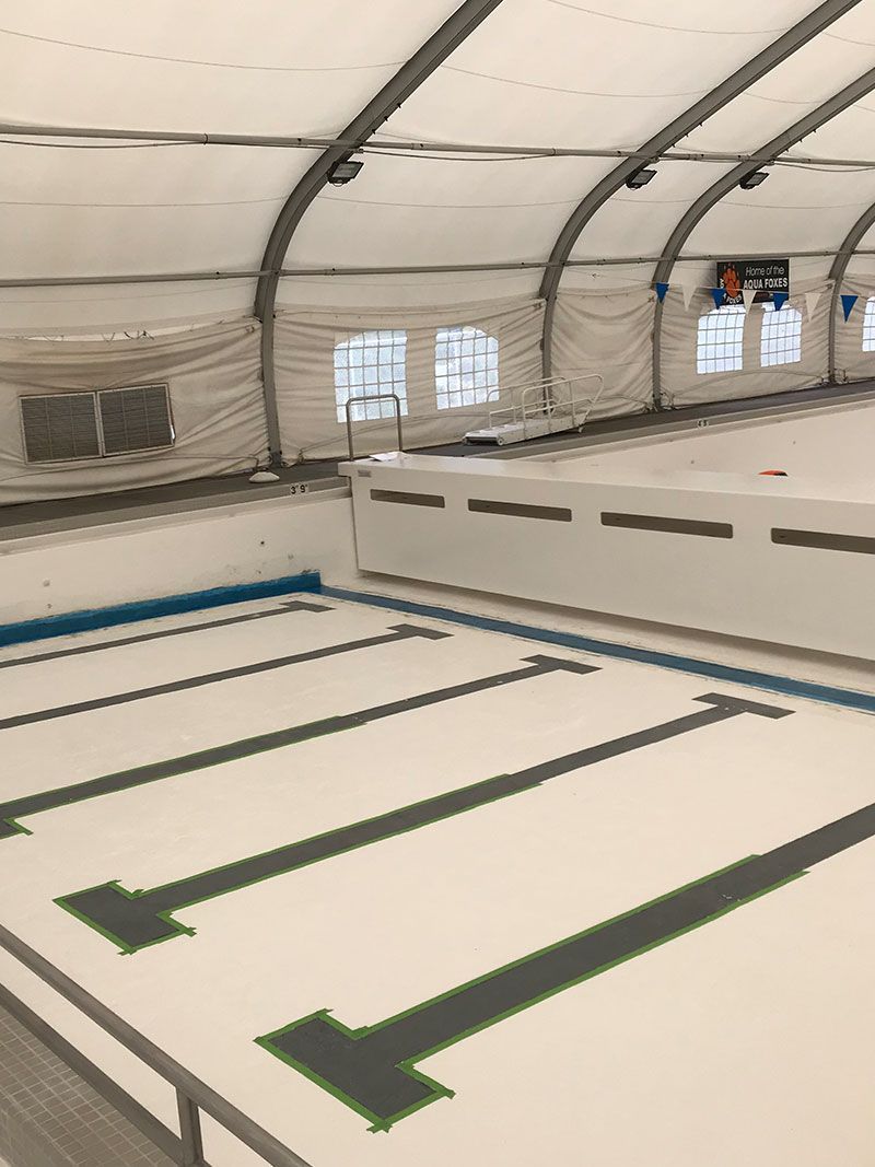 Indoor inflatable pool obstacle course with white lanes, green arrows, and a raised platform under a curved tent roof