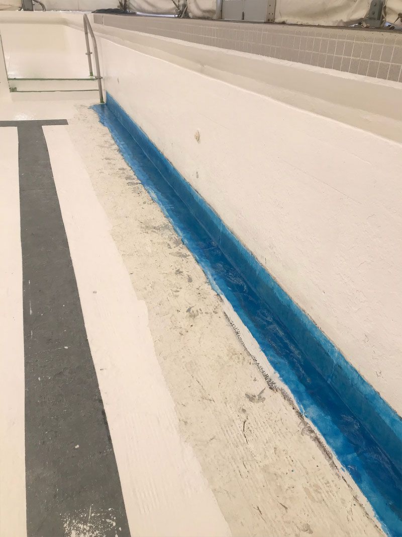 Blue painted line along a white indoor track lane and wall edge