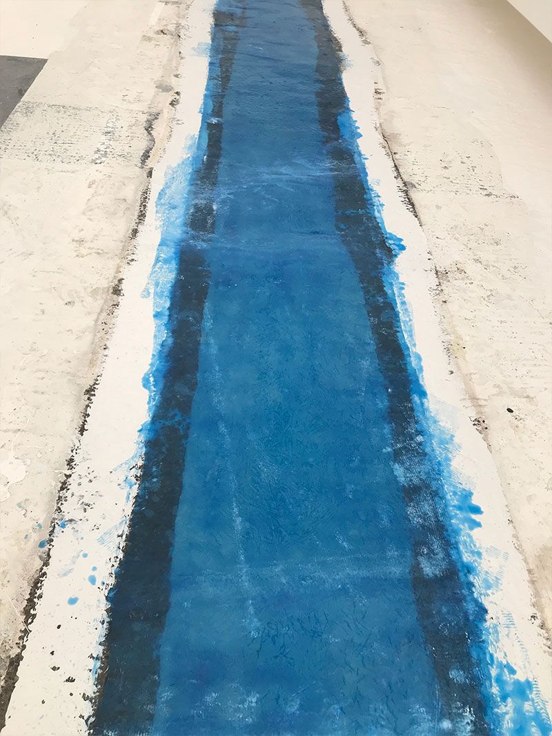 Blue painted strip on a light concrete floor, centered between rough white edges.