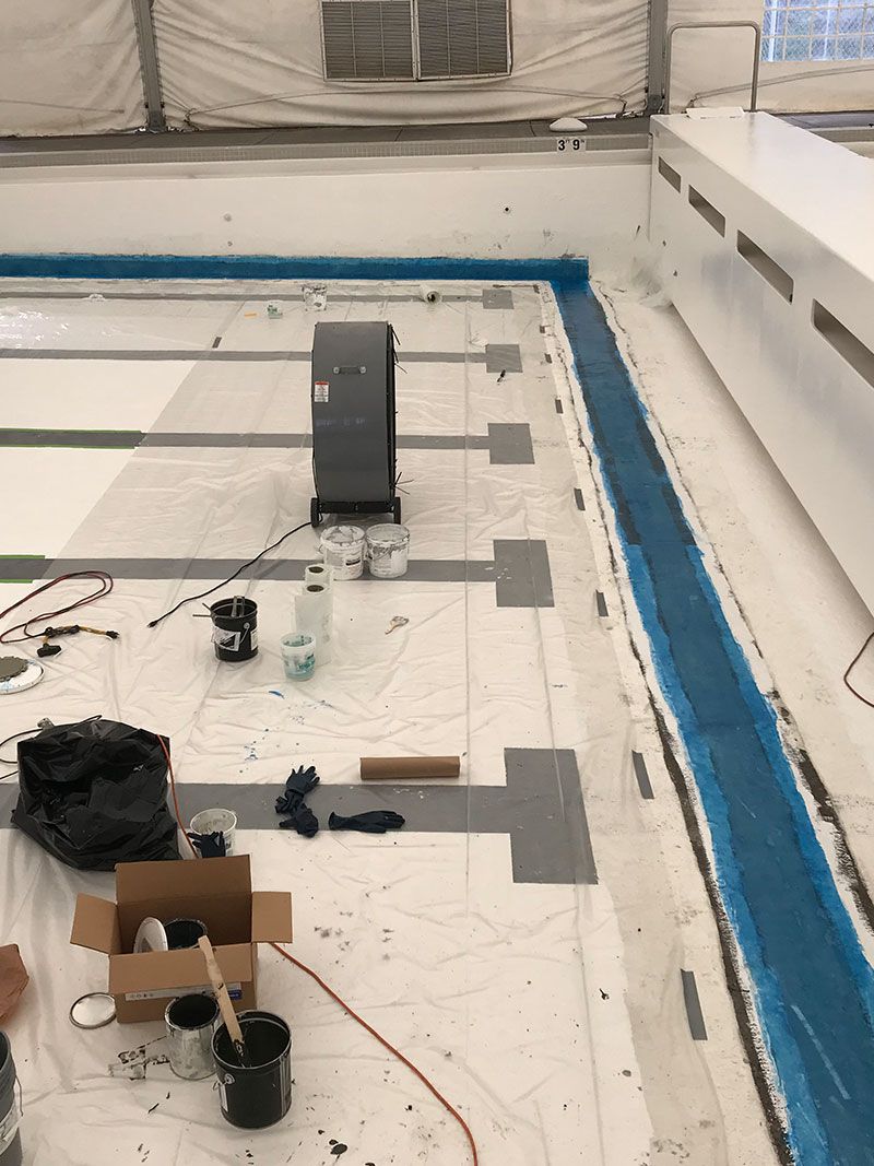 Rooftop with white flooring, blue perimeter strip, scattered tools and a black equipment box near center