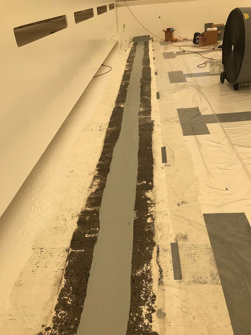 White indoor room with long black floor strips and taped markings near the wall.