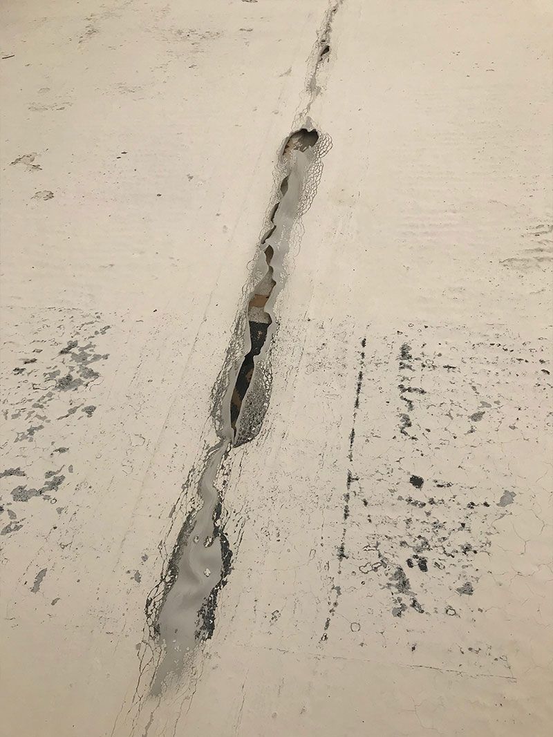 Vertical crack in a light-colored concrete surface with dark repair or erosion marks