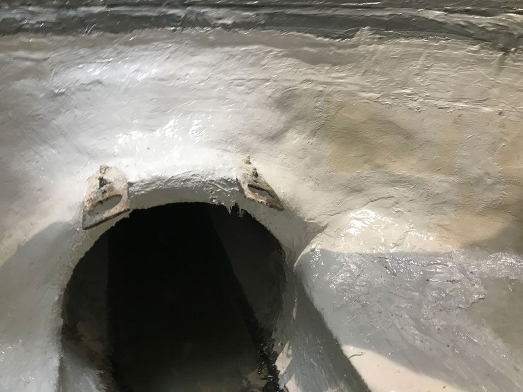 Close-up of a rough concrete tunnel opening with a dark interior and wet, reflective surface.