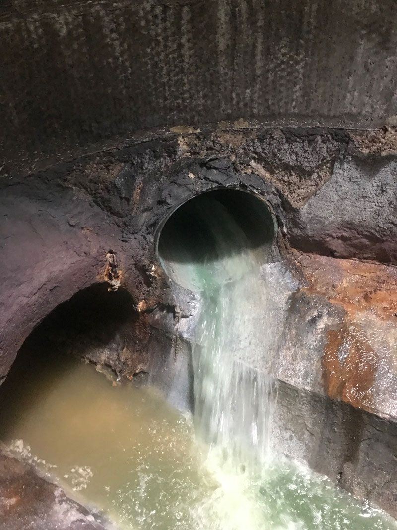 Dark drainage pipes releasing muddy water into a concrete ditch or culvert