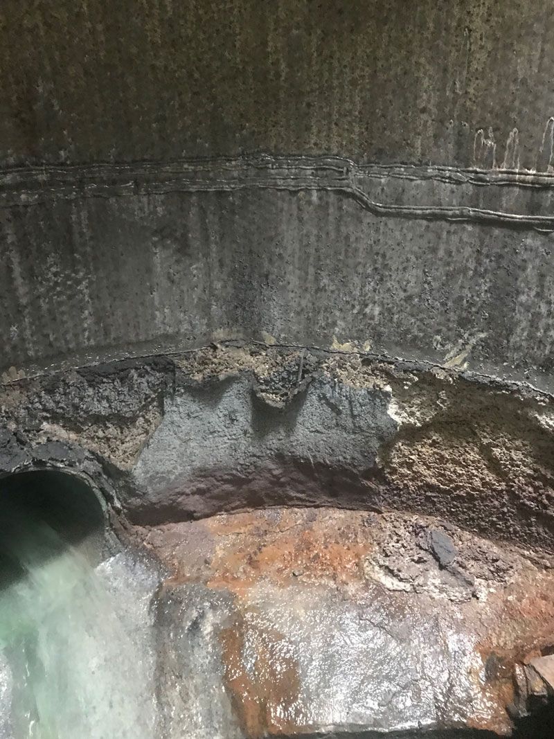 Rusty concrete drainage pit with water flowing from a pipe into a stained basin