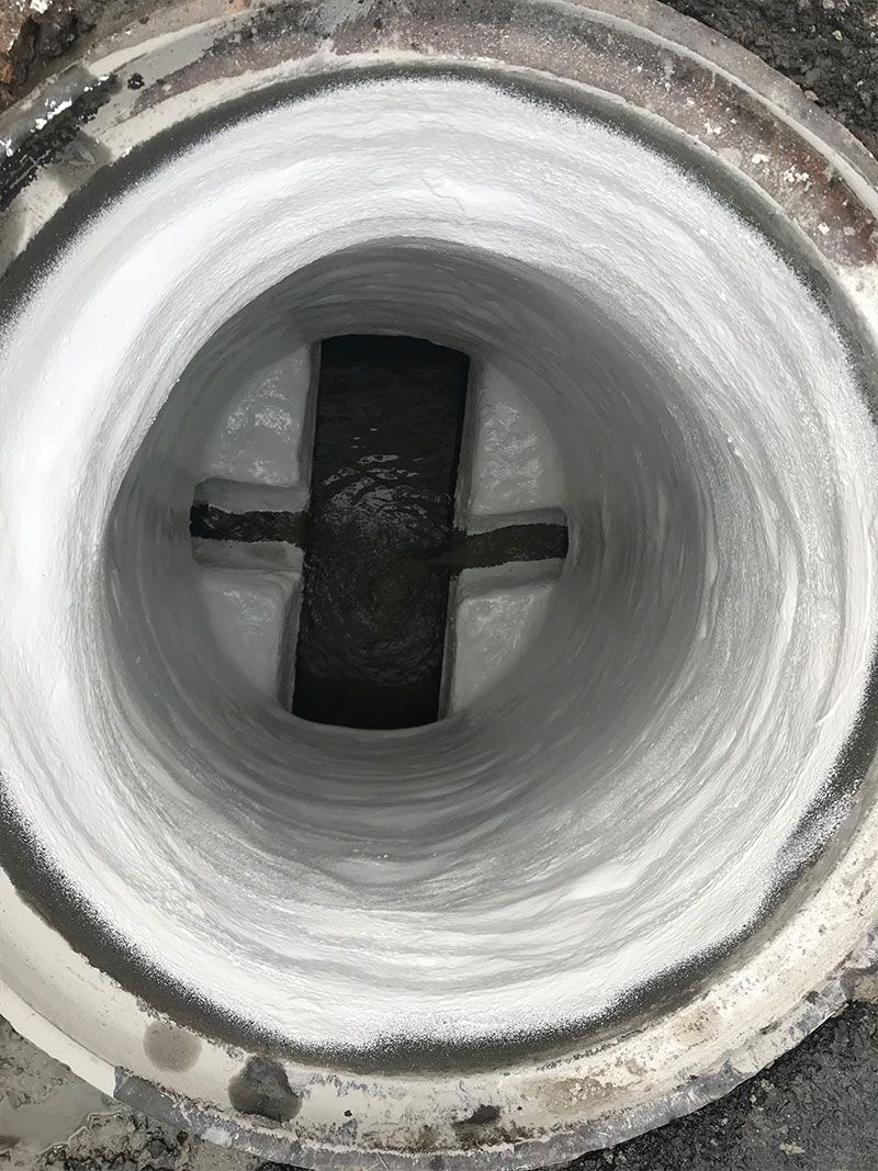 Close-up of a white circular pipe opening with a dark cross-shaped support inside.