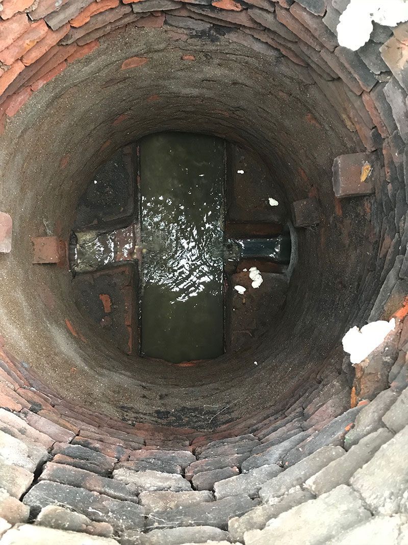 Looking down into a brick well with dark water at the bottom and some snow on the rim