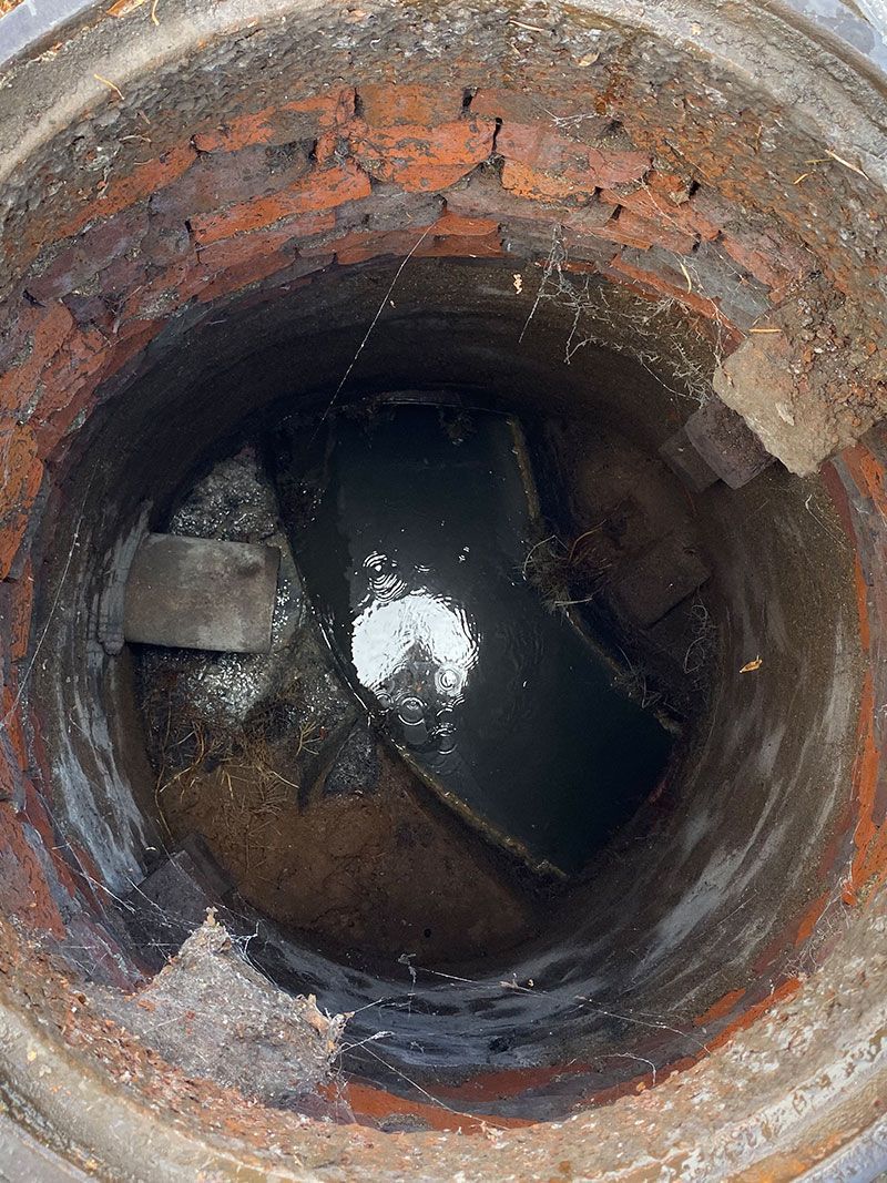 Corroded cylindrical drain or manhole interior with dark standing water at the bottom