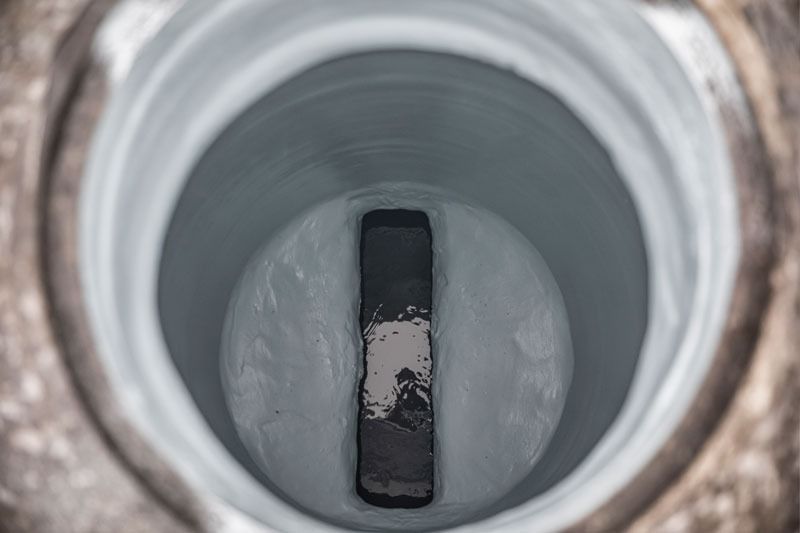 Inside a metal pipe, a dark rectangular object rests on the bottom amid white residue.