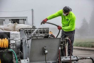 Worker in neon jacket spraying water on industrial equipment outdoors in foggy conditions