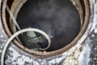 Cat peering out from inside a round metal pipe with steam or smoke around it