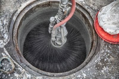 Industrial sewer pipe being cleaned with high-pressure water spray from a hose nozzle.