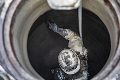 Worker climbing inside a large circular pipe, viewed from above.