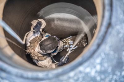 Worker in protective gear inside a large pipe, inspecting or repairing the interior.
