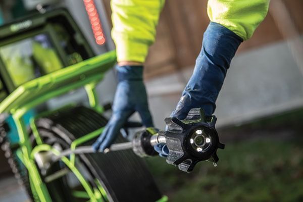 Person in neon jacket and gloves using a power drill on a green machine outdoors