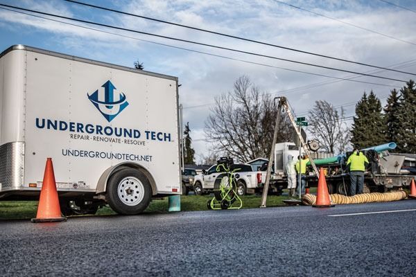 Underground tech trailer, utility trucks, cones, and workers on a roadside repair site