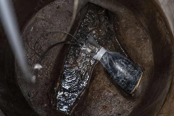 Wet black plastic bottle and metal object in a rusted bucket, viewed from above