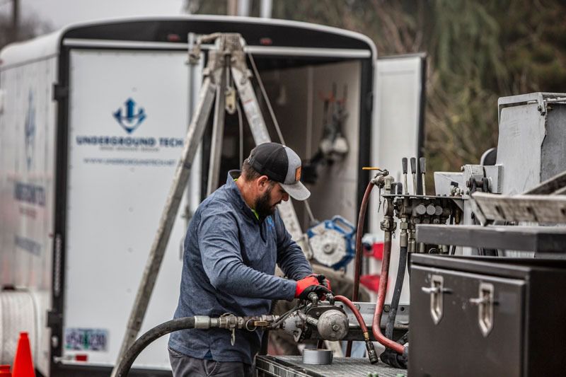 Worker in blue jacket operating equipment beside a truck in an industrial setting