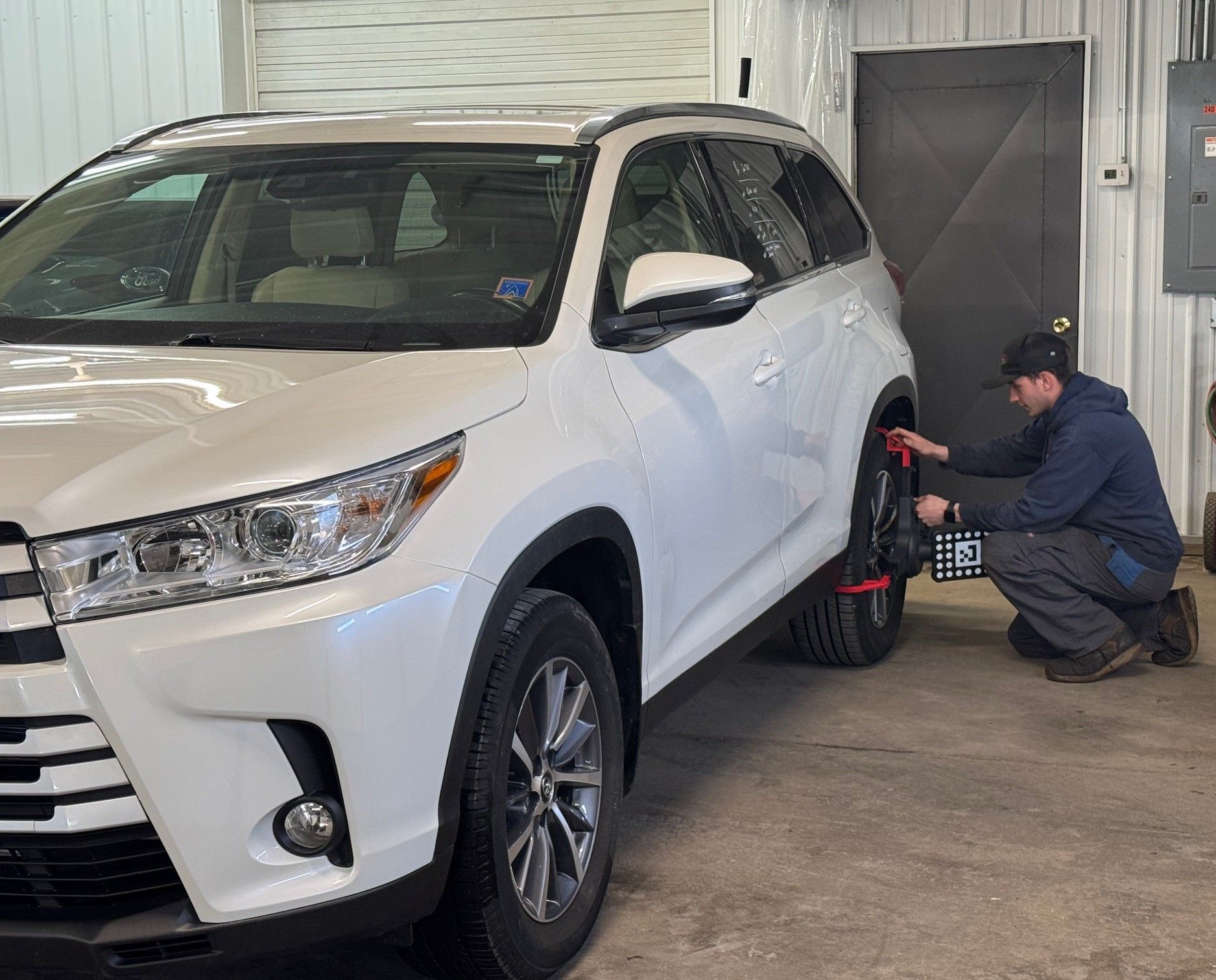 A man is kneeling next to a white suv in a garage.