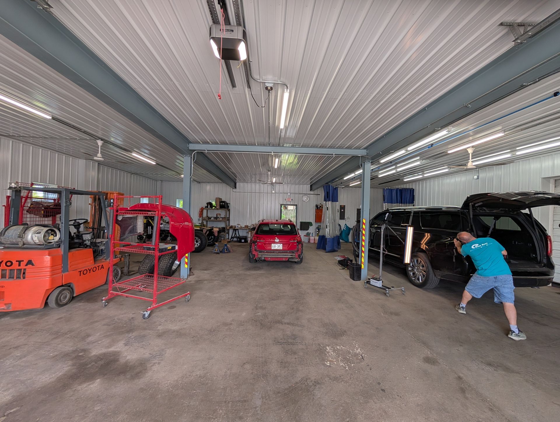 Auto repair shop with cars on lifts, a red forklift, and a person working near a black car.