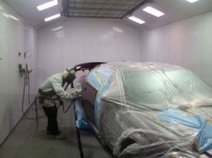 A man is painting a car in a paint booth.