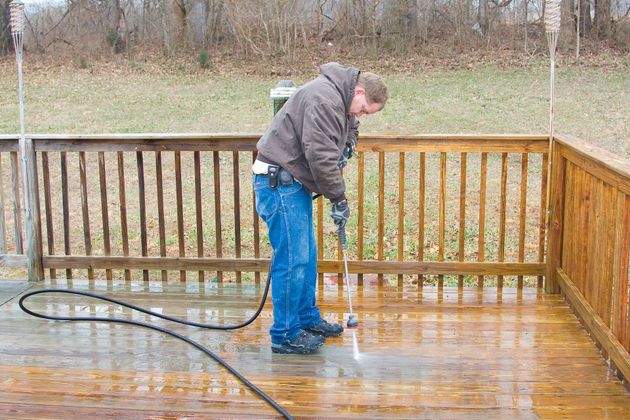 Person pressure-washing a wet wooden deck with a hose outdoors.