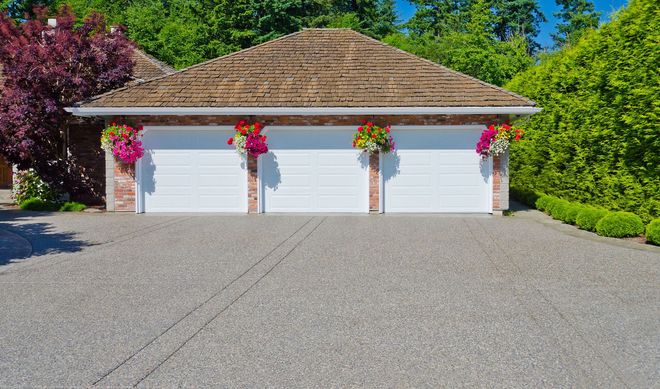Three-car garage with white doors, flower baskets, and a gravel driveway in bright sunlight