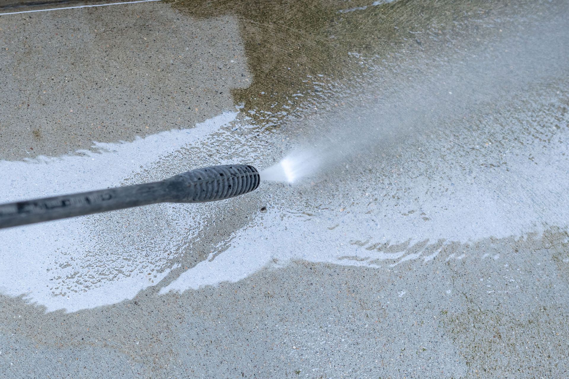 Pressure washer spraying water across a wet concrete surface