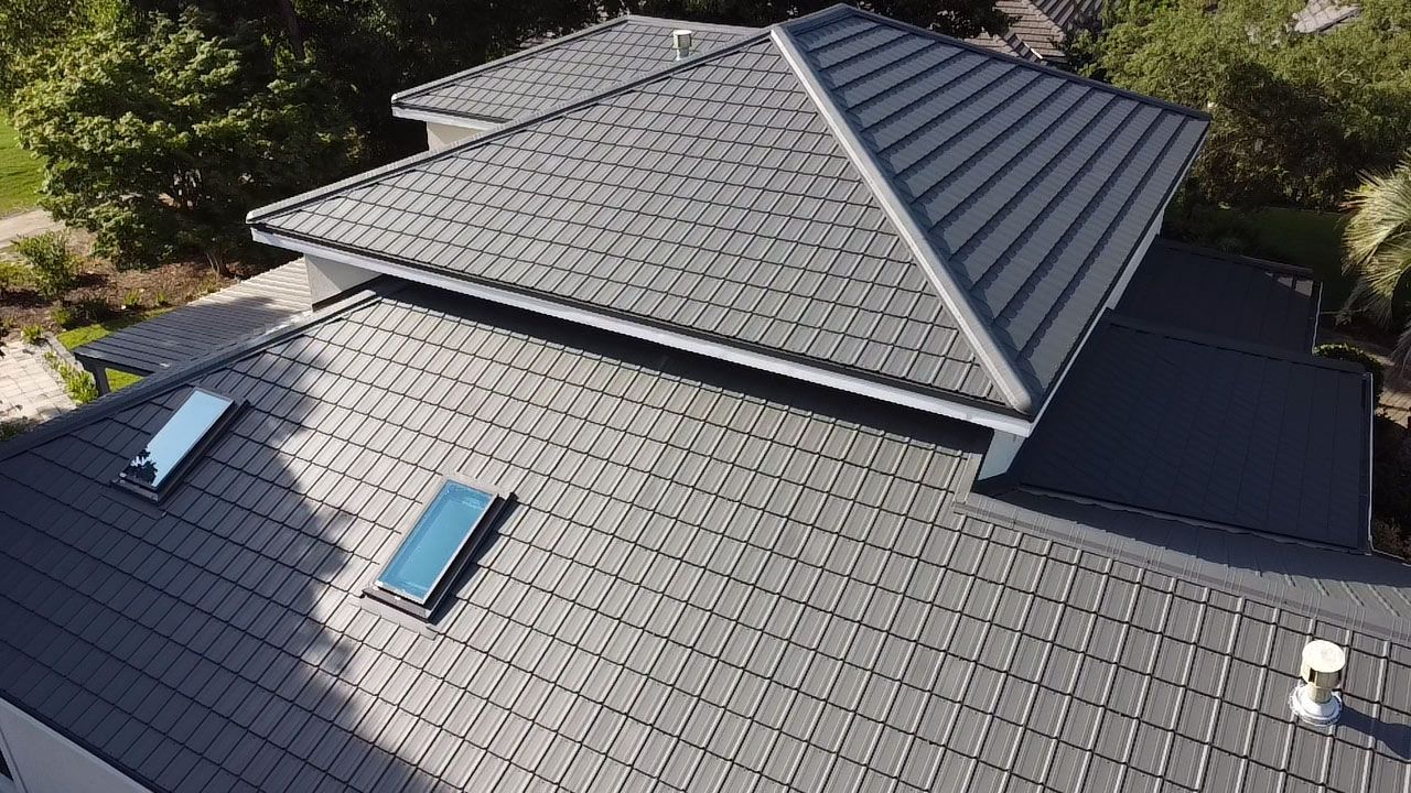 Aerial view of a dark gray shingled roof with two skylights and a raised central section.