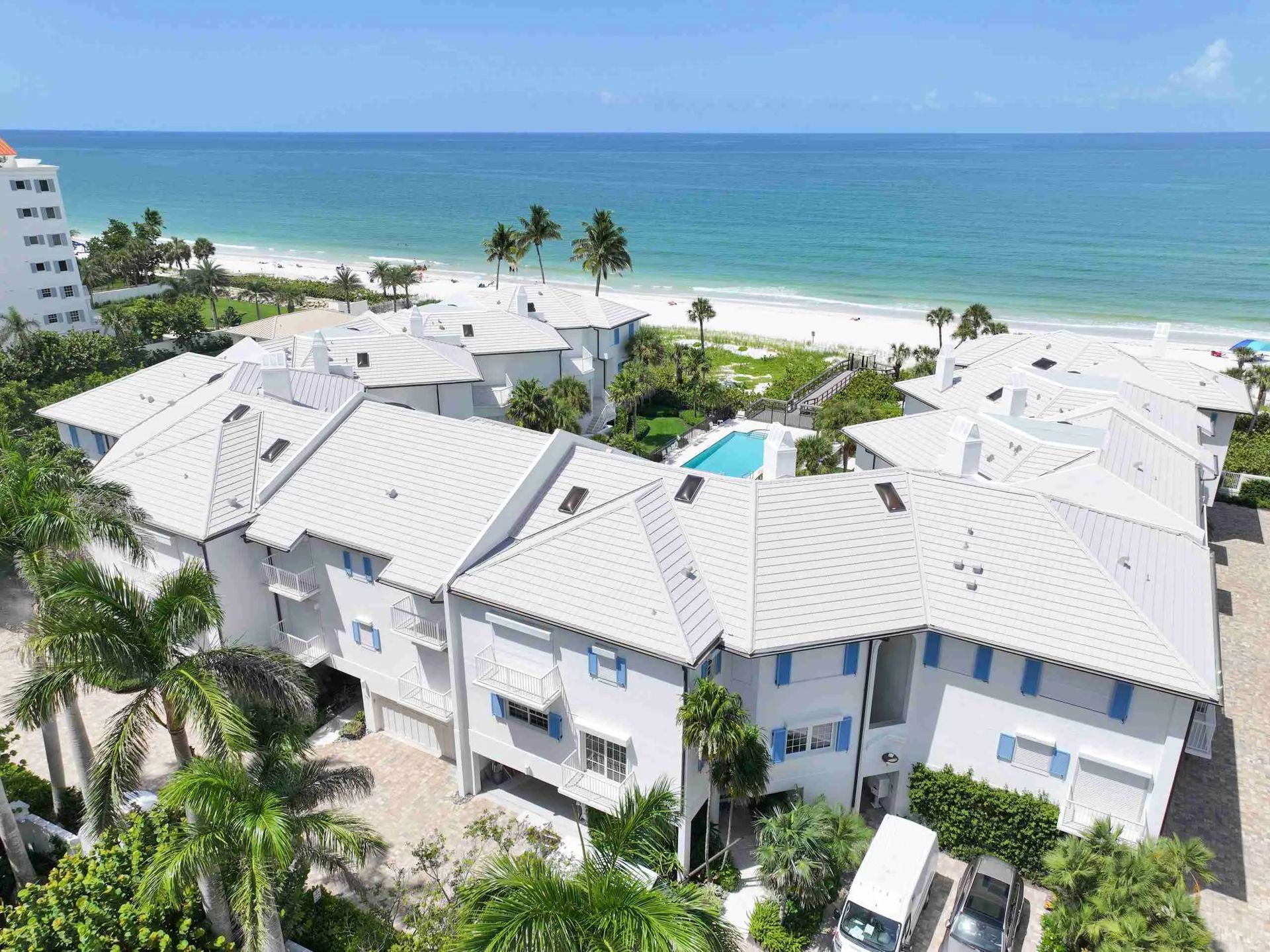 White beachfront condos with palm trees overlooking a turquoise ocean under a clear blue sky