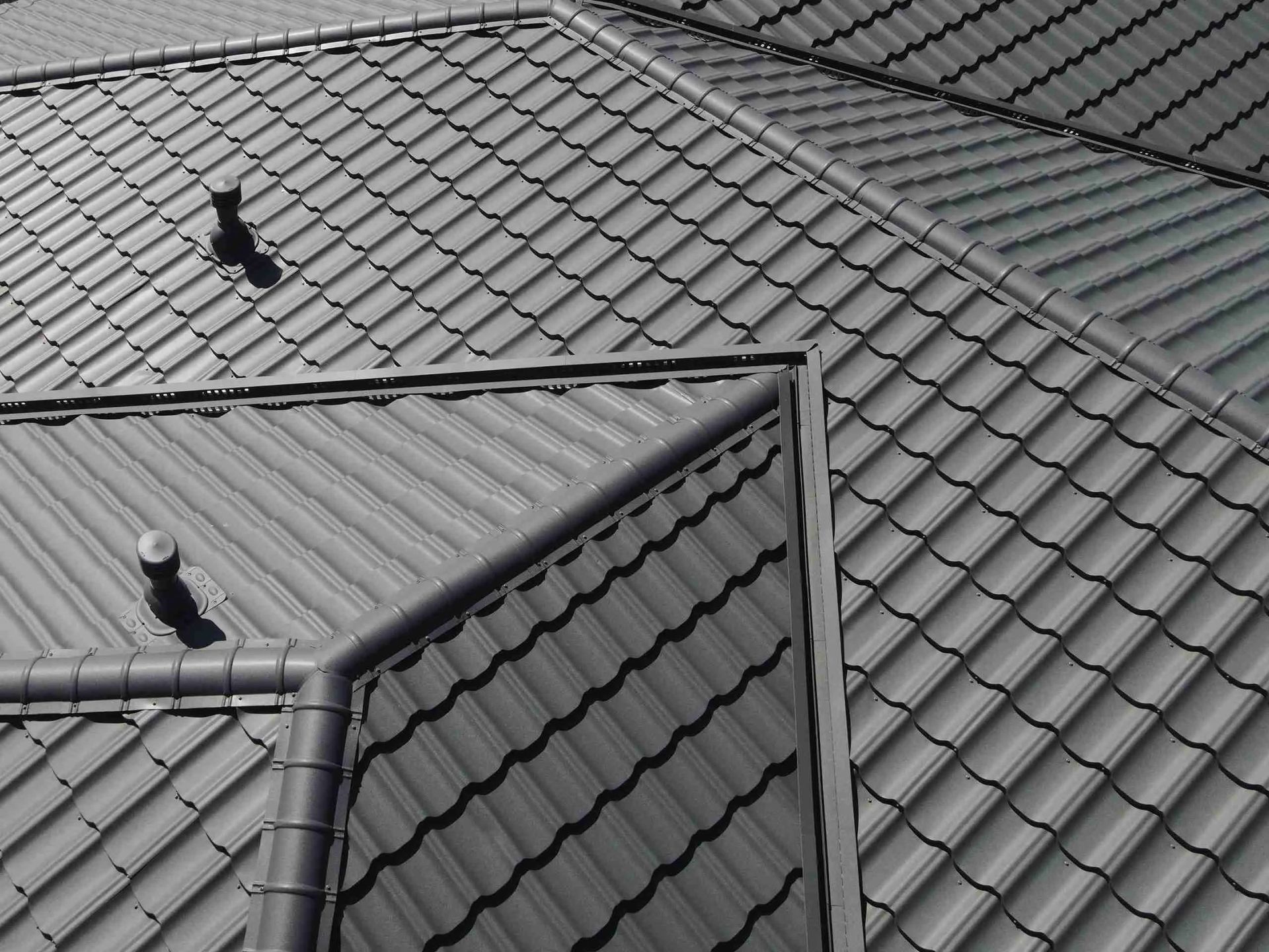 Gray tiled roof with two small roof vents and a corner gutter system