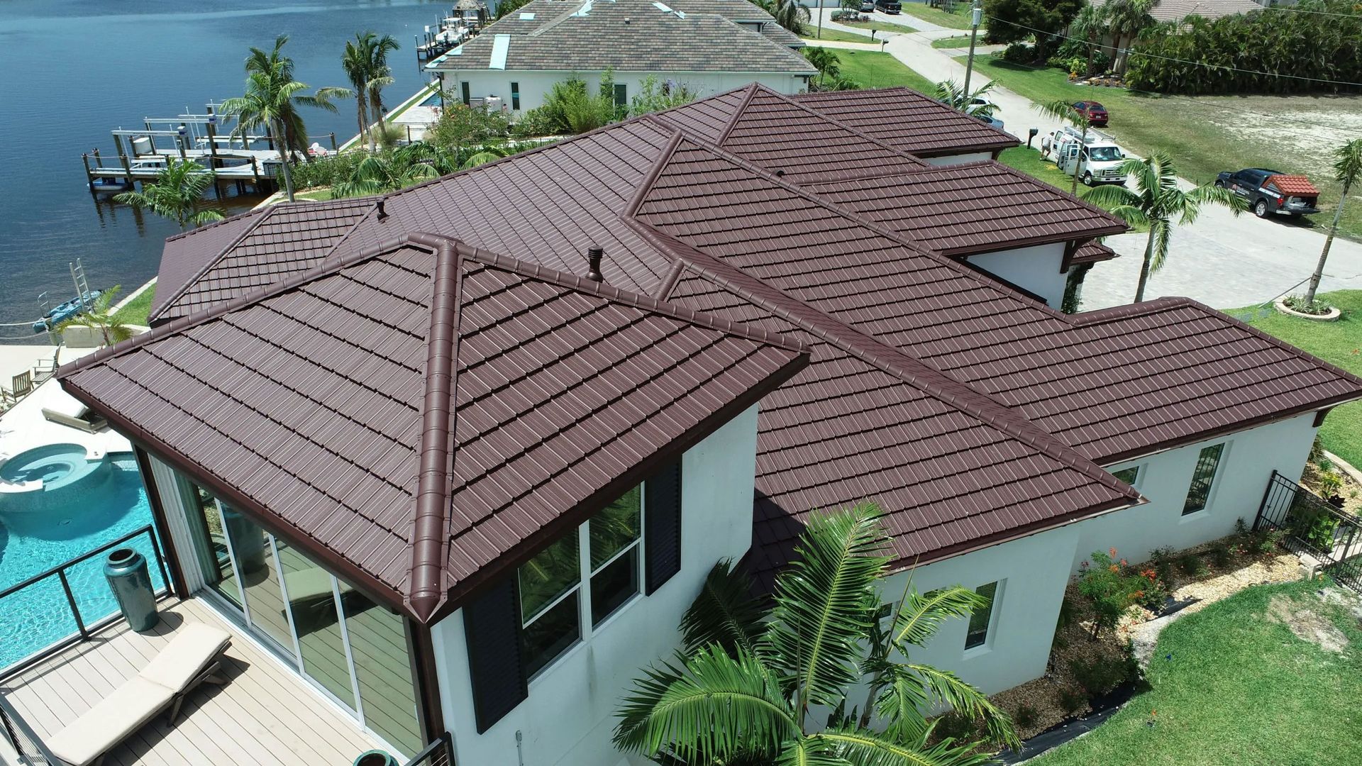 Aerial view of a tropical resort villa with brown tiled roofs, pool, palm trees, and ocean nearby