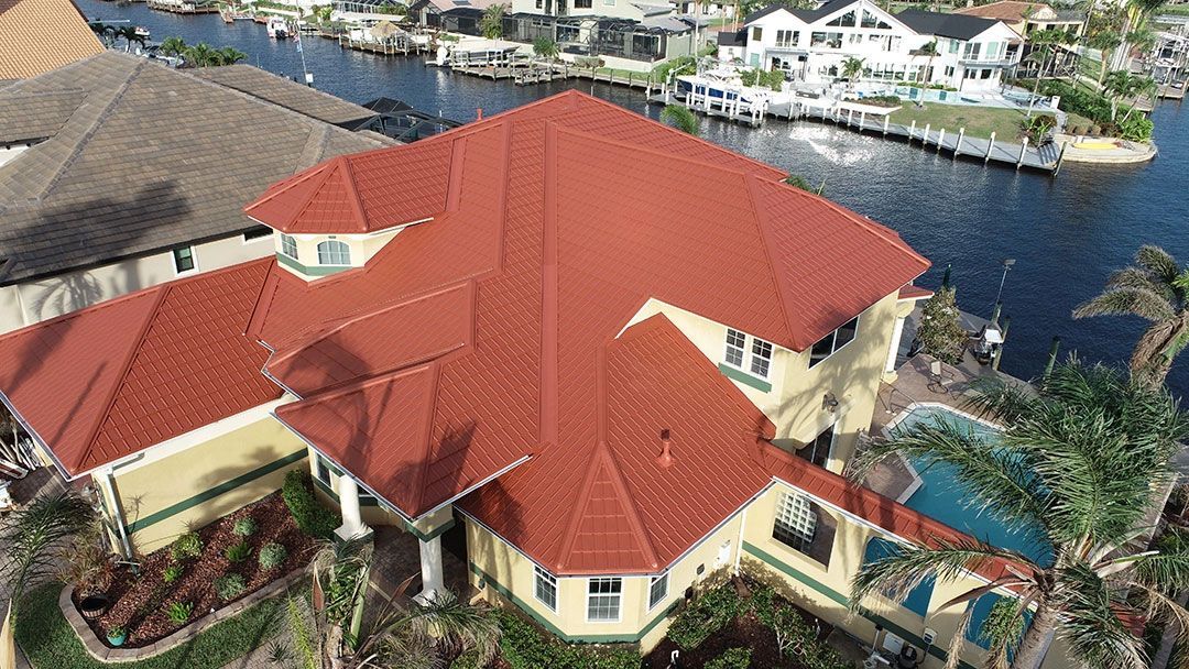 Aerial view of a large red-roofed waterfront house beside a canal with docks and neighboring homes.